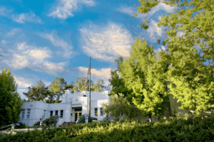 White building with grass, trees and blue sky with clouds above