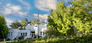 White building with grass, trees and blue sky with clouds above